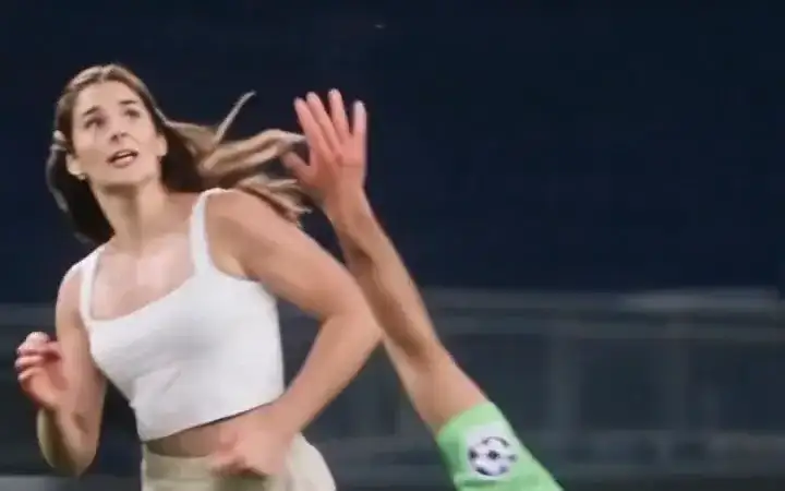 A woman in a white top lifts the ball over a diving green goalkeeper