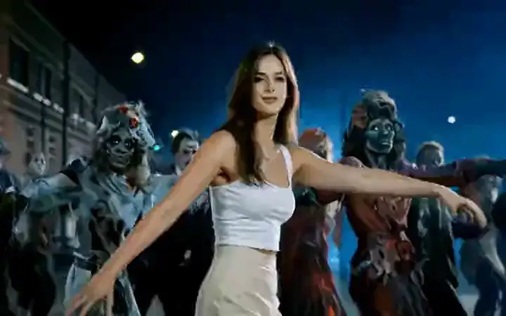 A woman in a white top leads a zombie crowd down a night street