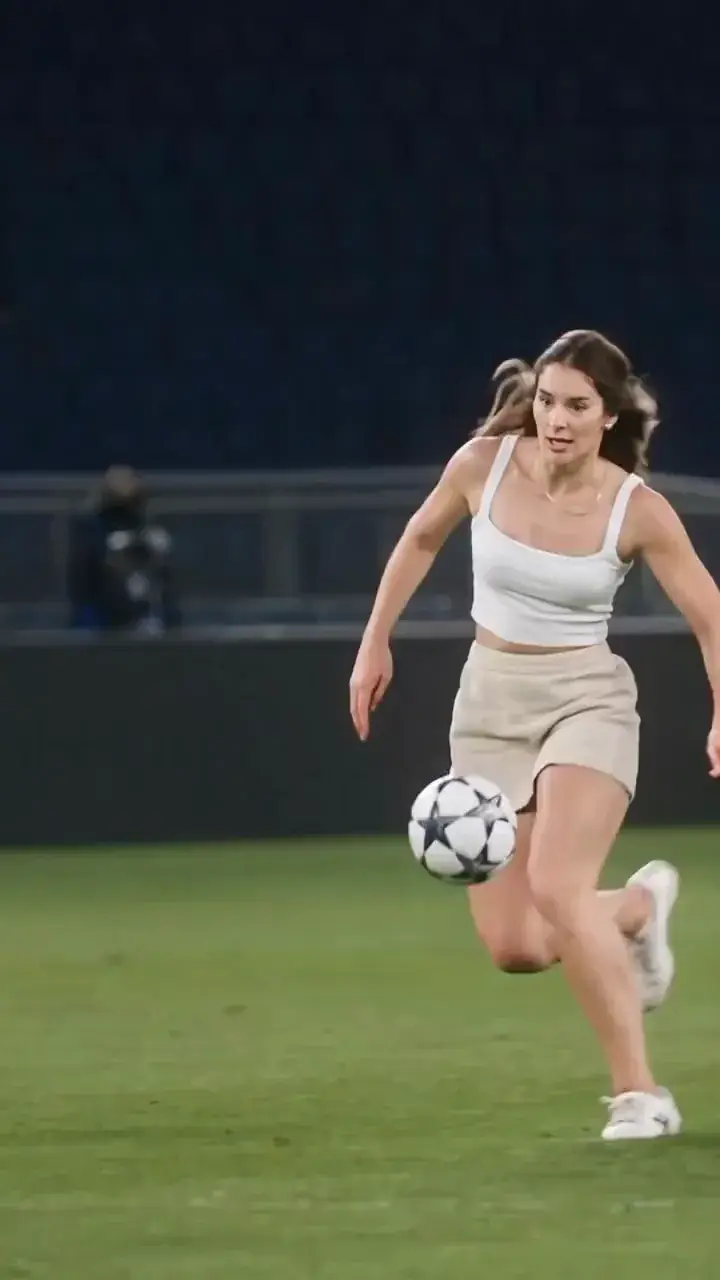 MixVio sample of a floodlit goal: a woman in a white top and beige skirt chips a green goalkeeper, then finishes into the empty net