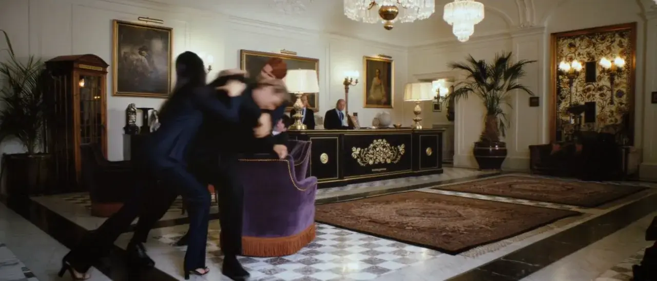Ultrawide hotel lobby video where two people struggle beside a purple chair.